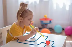 Liten jente som blåser en kule gjennom en labyrint. Hun har på seg gul kjole