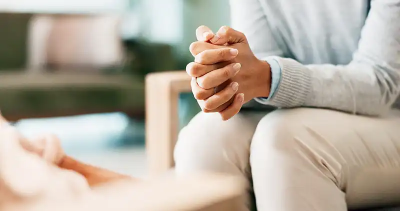 Delbilde av en dame som sitter med foldete hender på lårene
